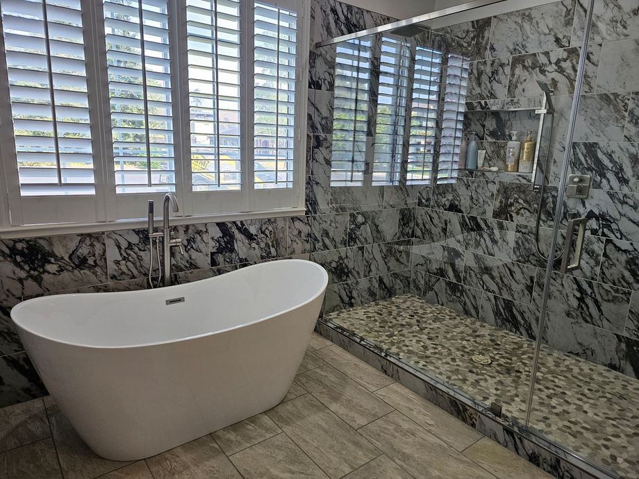 Modern bathroom with a white freestanding tub, marble tile walls, and a pebble-tile shower