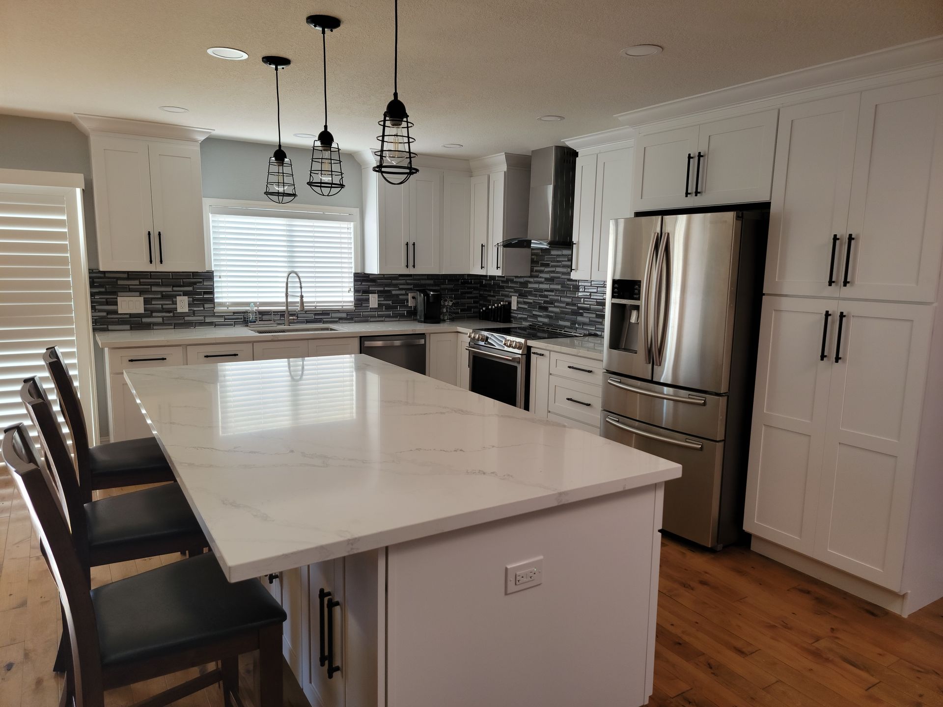 Bright modern kitchen with white cabinets, stainless fridge, island seating, and pendant lights