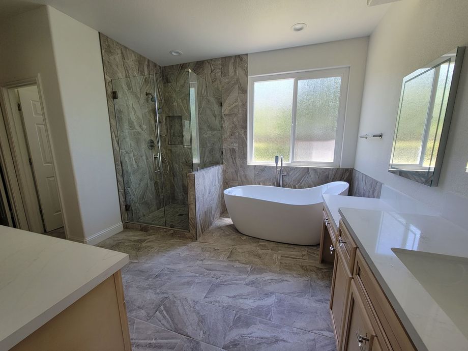 Modern bathroom with freestanding tub, marble shower, double vanity, and large window