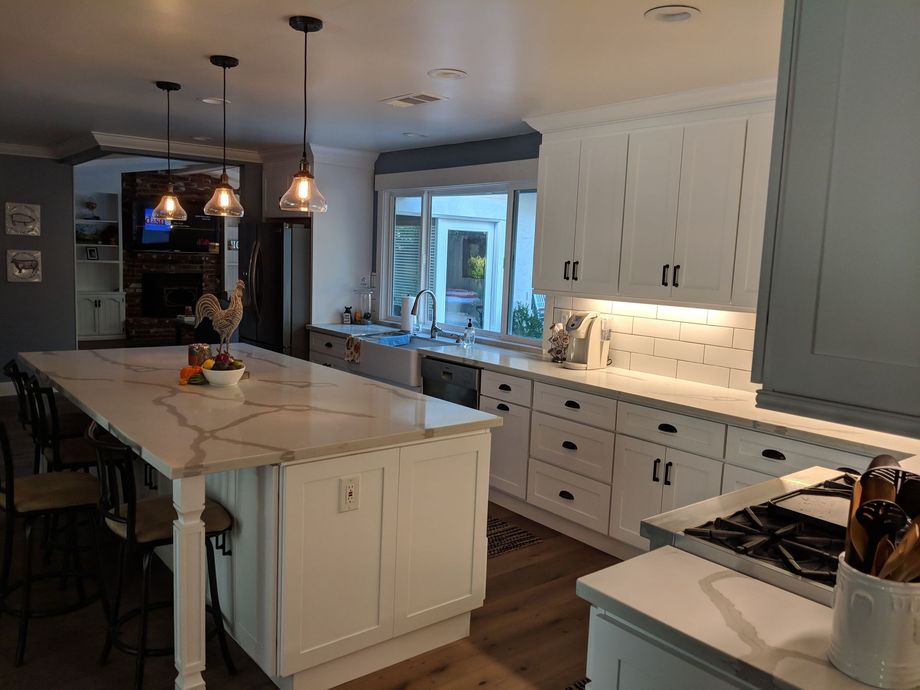 Bright modern kitchen with white cabinets, marble island, pendant lights, and a window over the sink