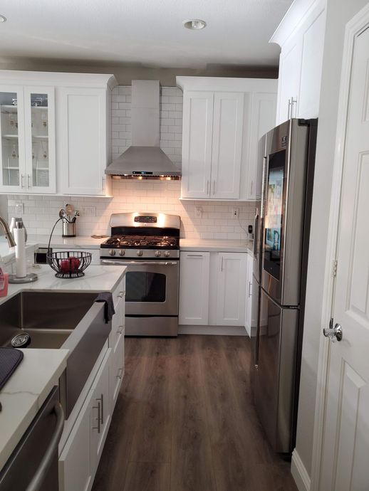 Bright white kitchen with stainless steel appliances, white cabinets, and wood-look flooring.