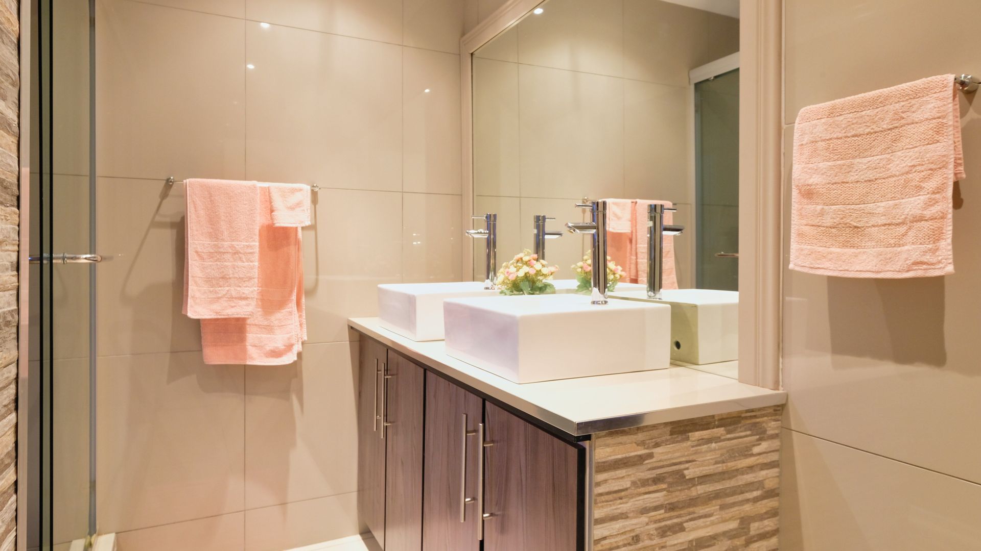 Modern bathroom with glass shower, white tile, and gray built-in cabinets