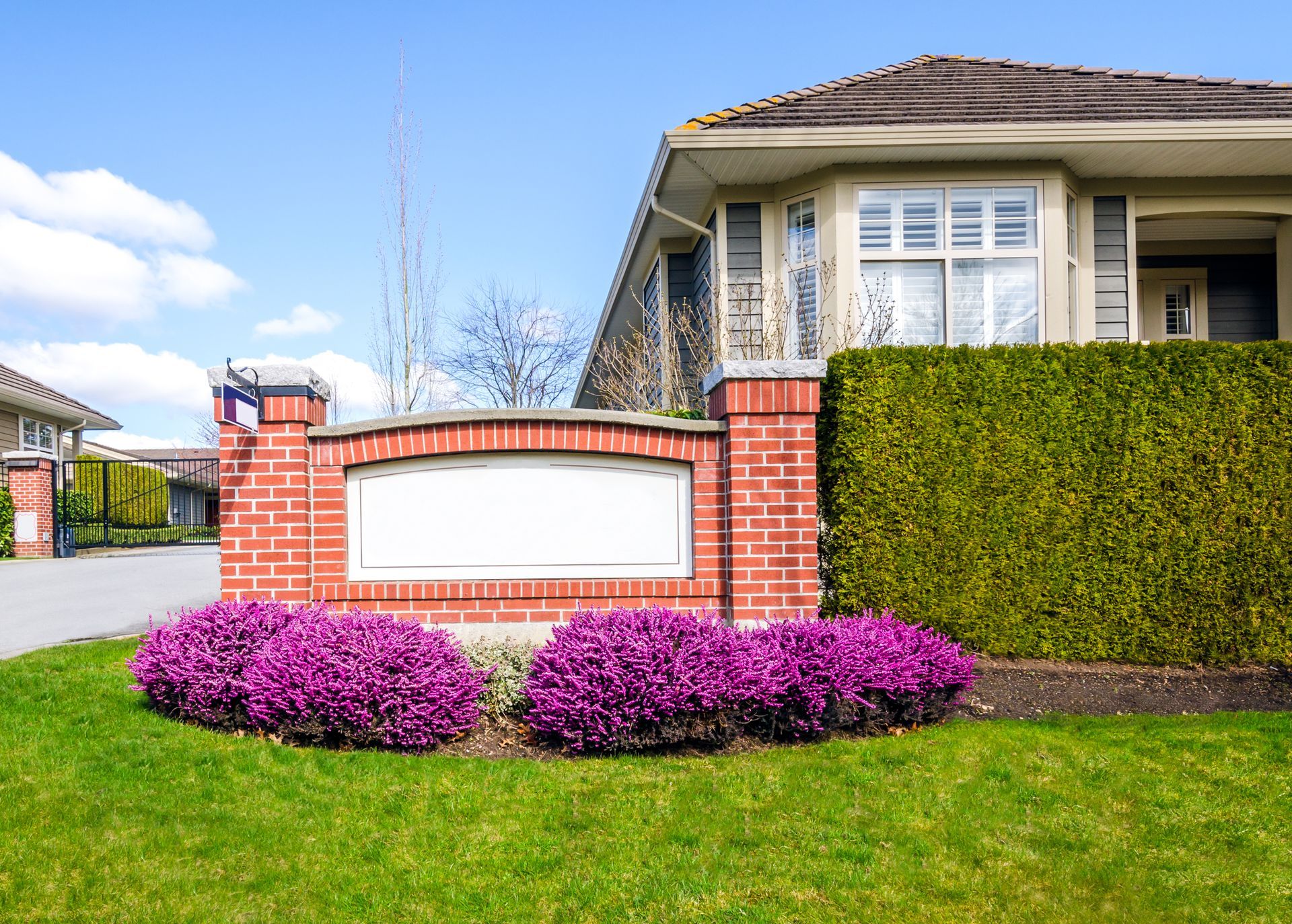 Brick entrance sign with blank space, flanked by pink flowers and green hedge.