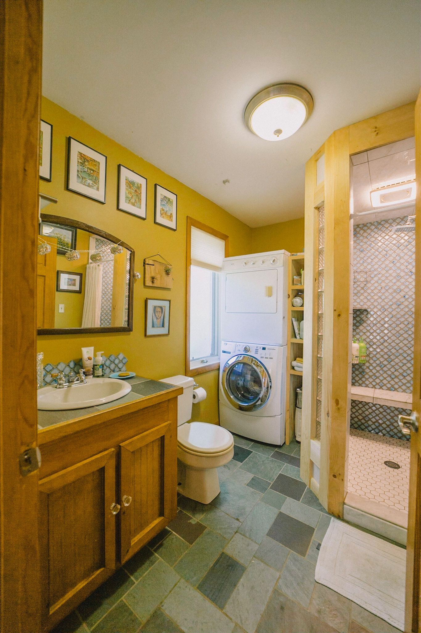 Bathroom with golden yellow walls, wooden cabinetry, and a stacked washer and dryer unit.