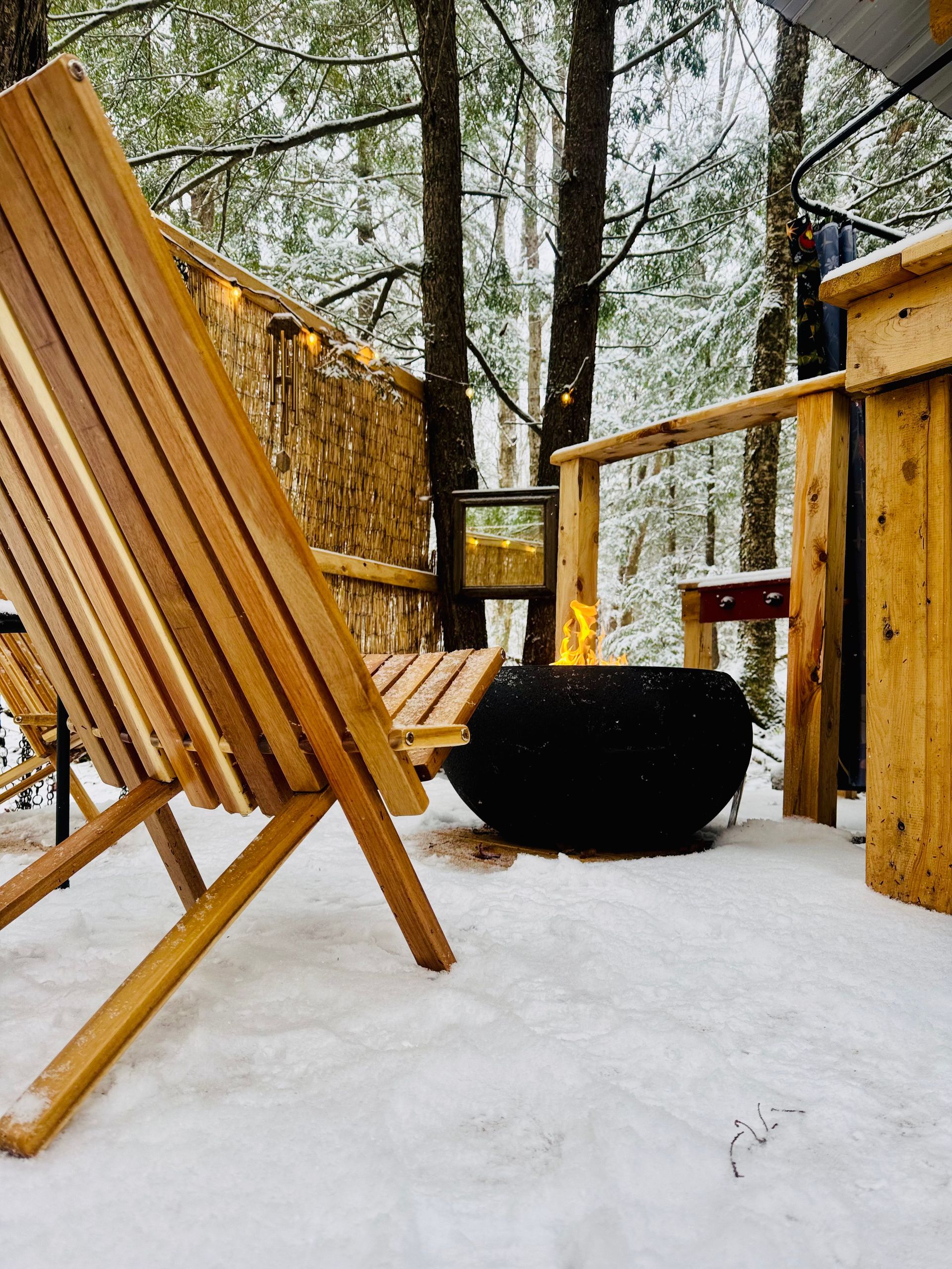 Wooden chairs around a fire pit in a snowy forest.
