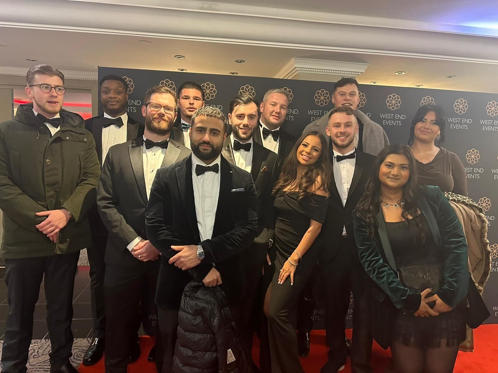 Group of people dressed for a formal event, posing together in front of a black-and-gold backdrop.