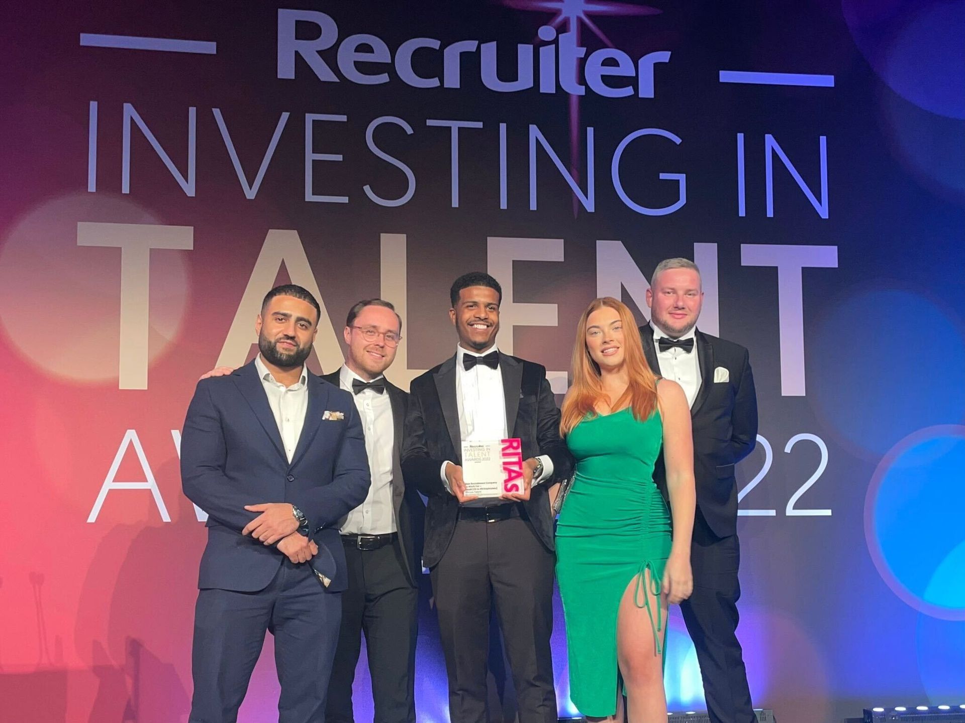 Five people pose on stage at the Recruiter Investing in Talent Awards, holding an award.