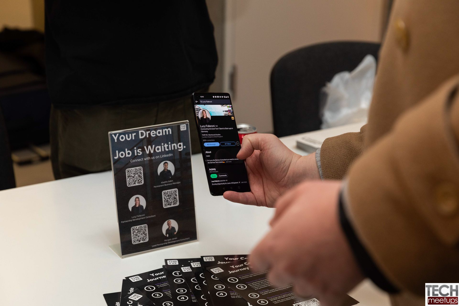 Person using a smartphone to photograph a table display with “Your Dream Job is With Us” sign at a job fair