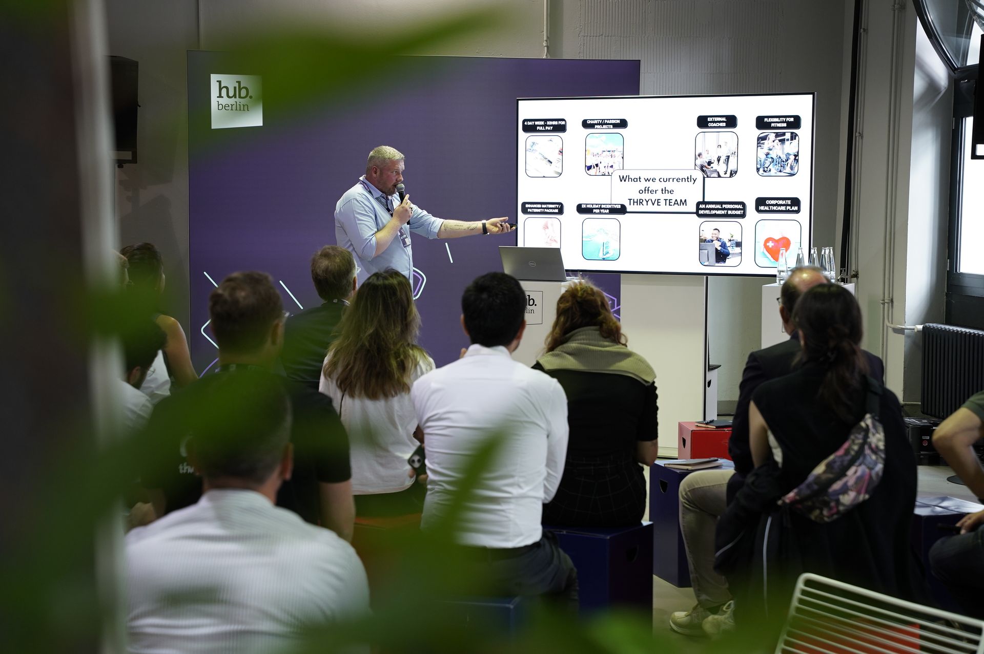 Presenter speaking to an audience in a conference room beside a large display screen.