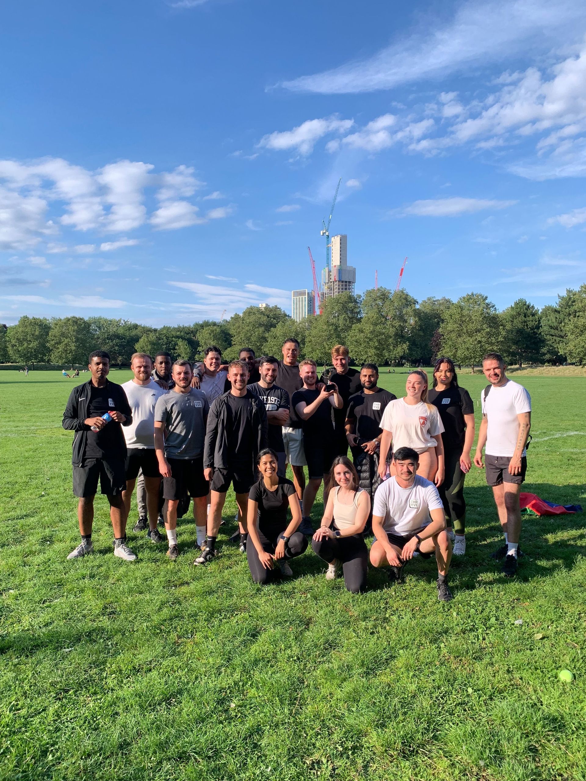 Group of people posing on a grassy field with a city skyline and blue sky in the background