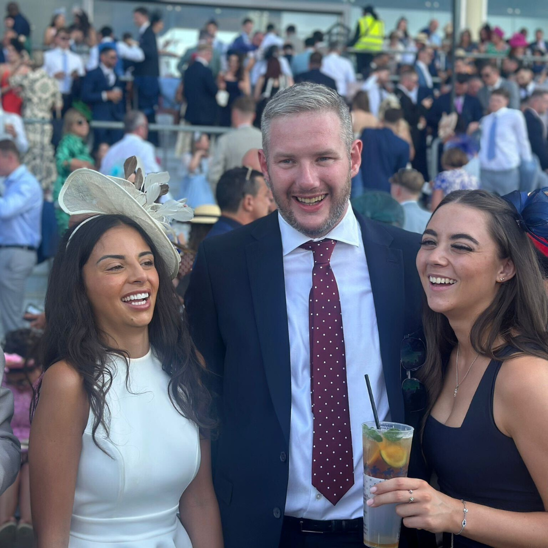 Three people smiling at an outdoor event, with a crowd blurred in the background.