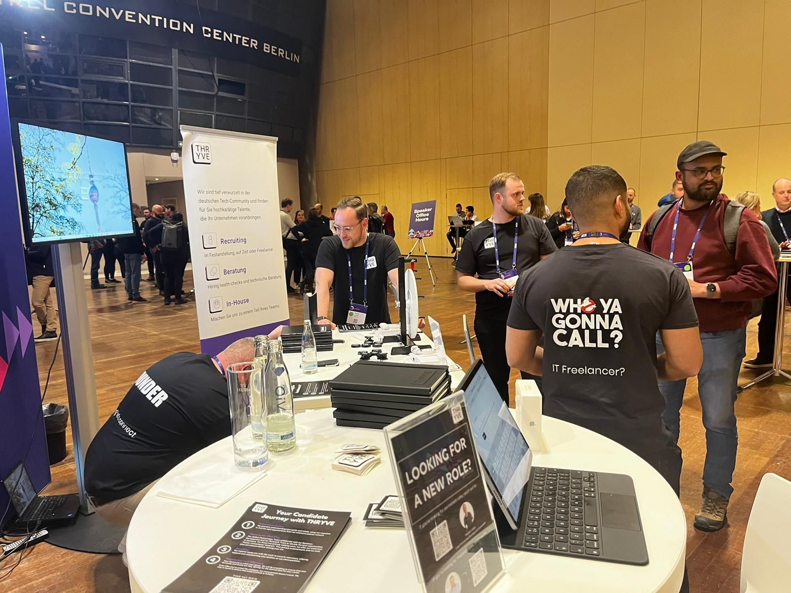 Convention booth with people networking around a white demo table and monitors in a busy exhibition hall