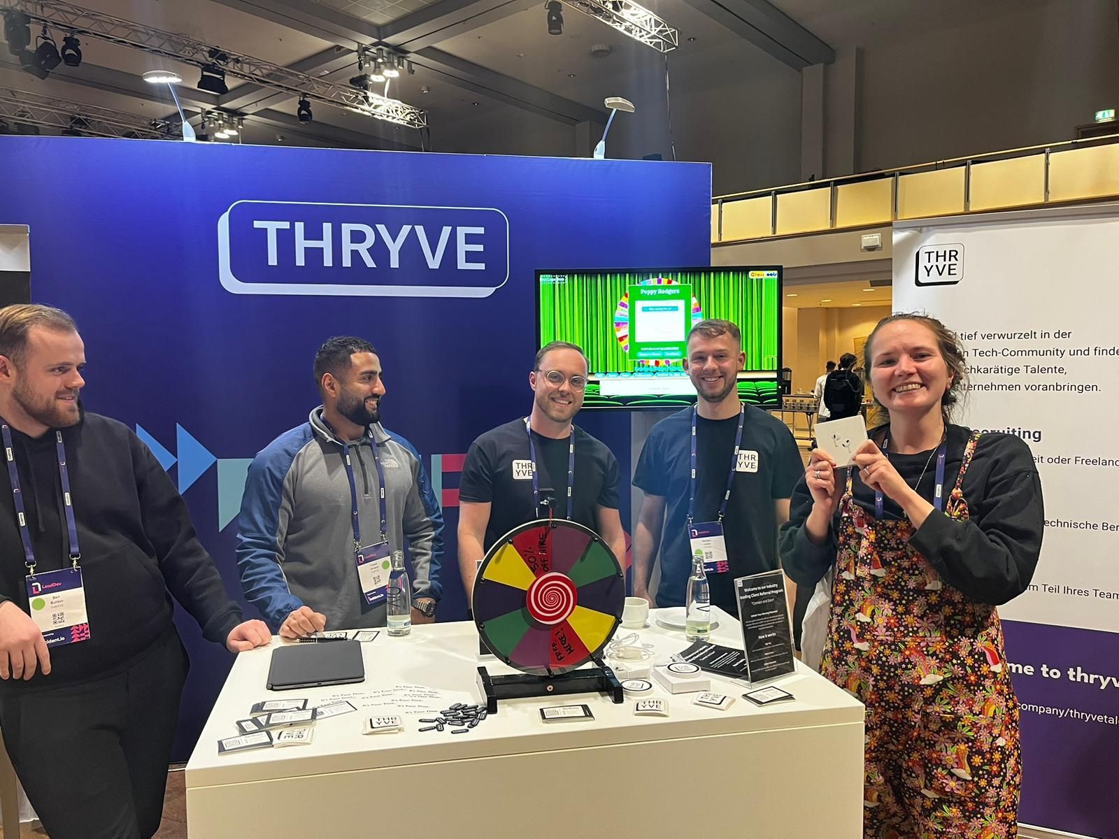 People at a THRYVE trade booth holding a trophy beside a colorful prize wheel and display table