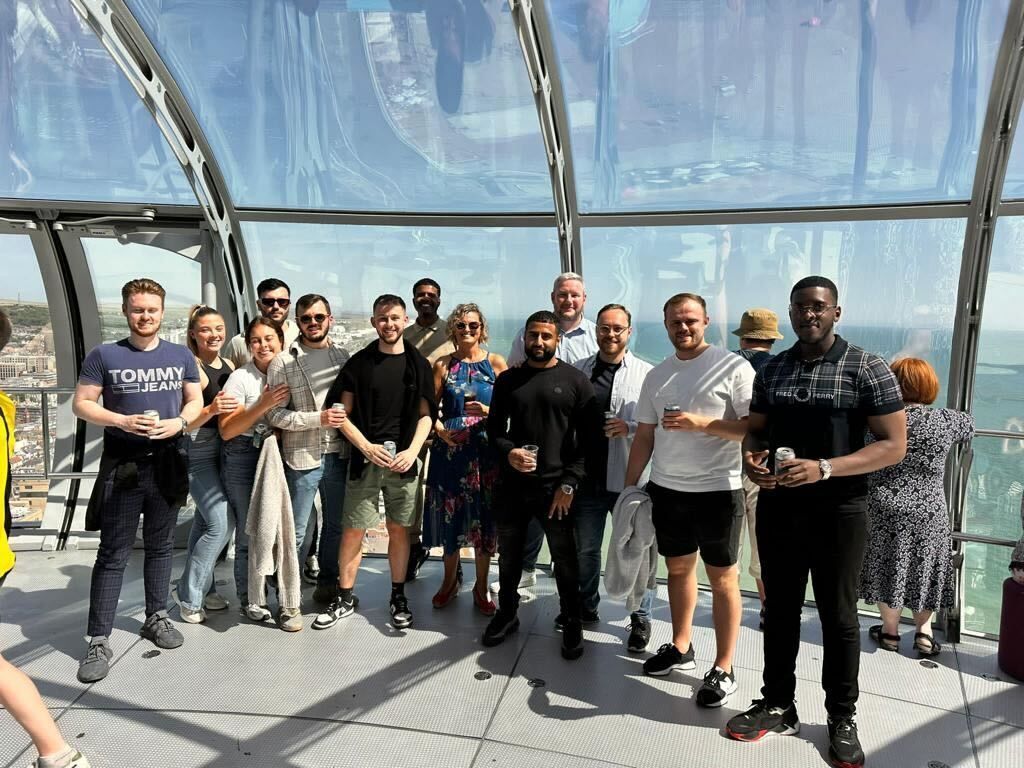 Group of people posing in a glass observation deck with city views, smiling at the camera.