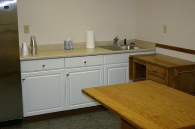 Small kitchen area with white cabinets, sink, wooden table, and wooden chest.