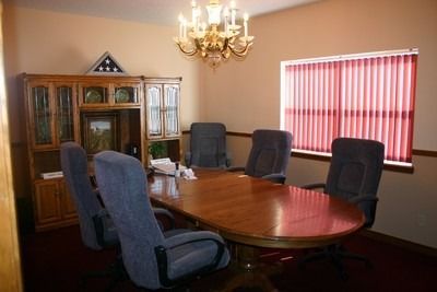 Conference room with oval wooden table, dark chairs, chandelier, display cabinet, and window blinds