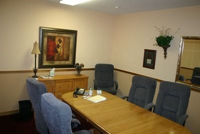 Conference room with wooden table, blue chairs, cabinet, lamp, and wall art.