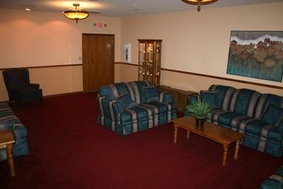 Empty lobby with red carpet, blue plaid couches, wooden tables, and wall art.