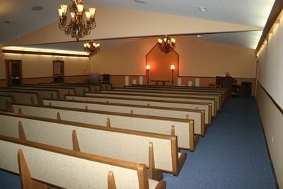 Empty church sanctuary with rows of wooden pews, blue carpet, and chandeliers under warm lighting