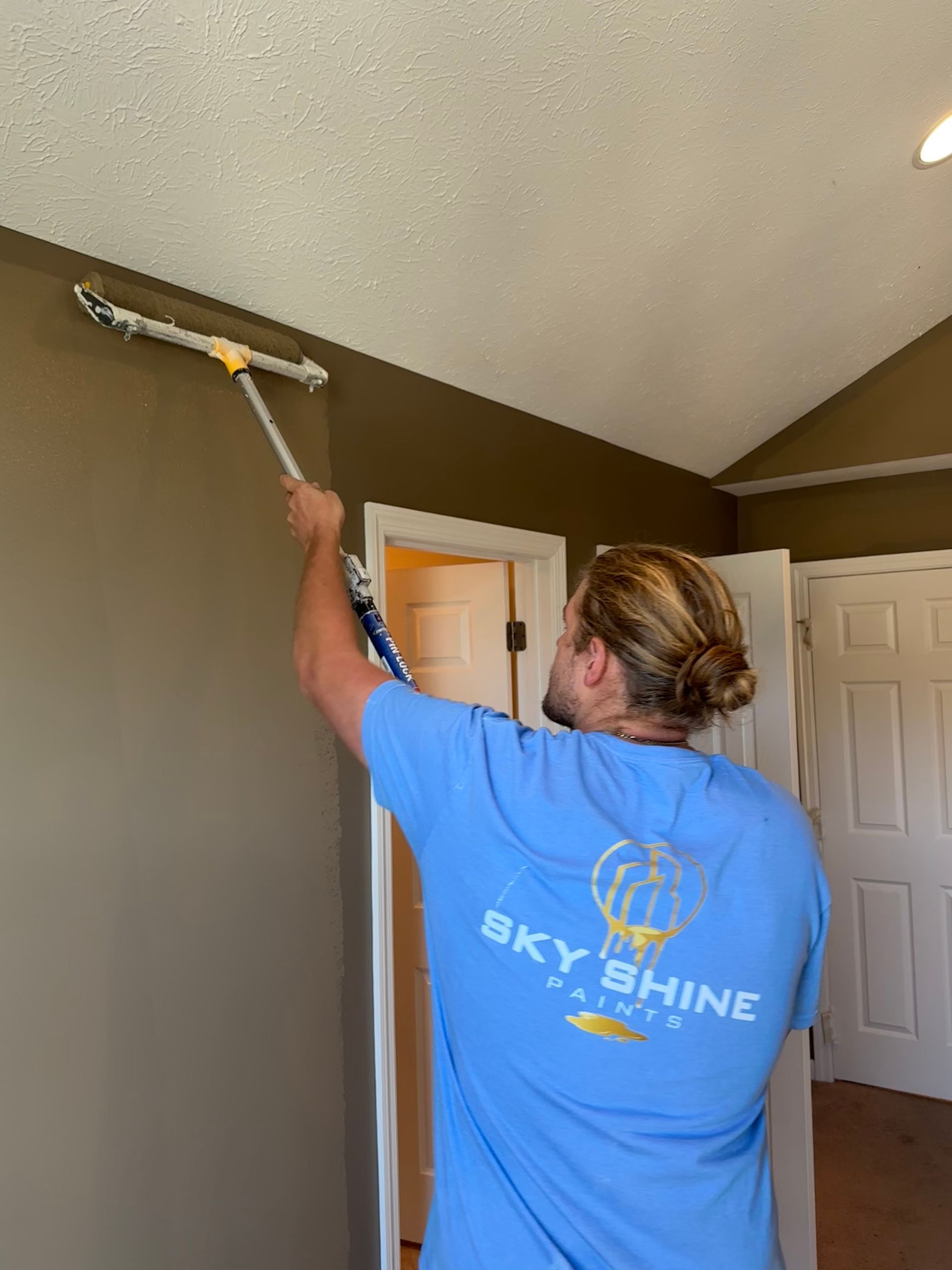 A man in a blue shirt is cleaning a wall with a mop.