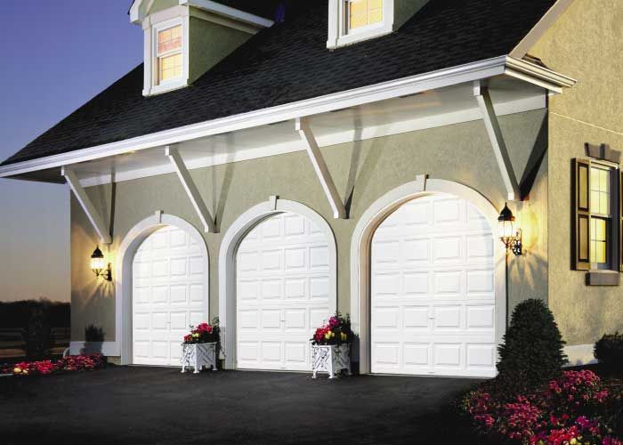 Una casa con tres puertas de garaje arqueadas y techo negro.