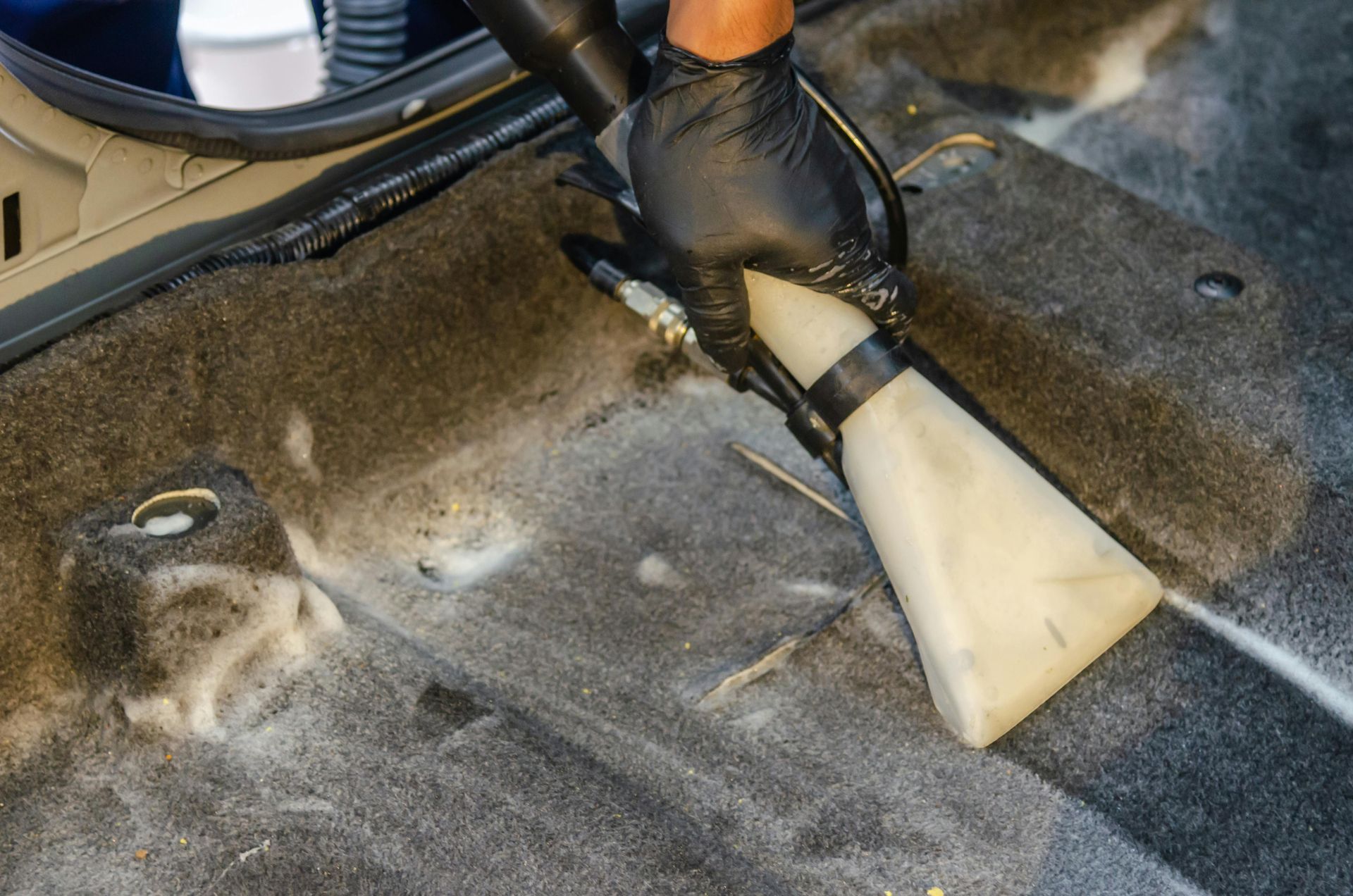 Person using a vacuum attachment to clean a car’s dirty floor carpet
