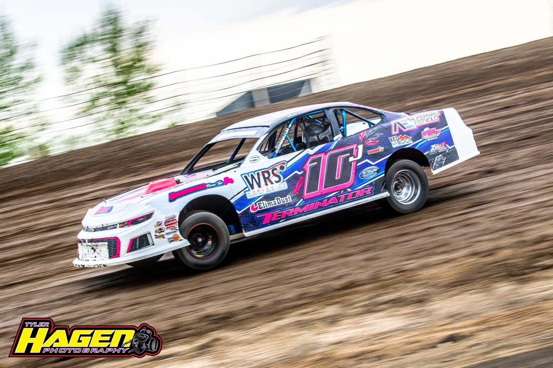 White and blue dirt track race car drifting on a muddy track with sponsor decals