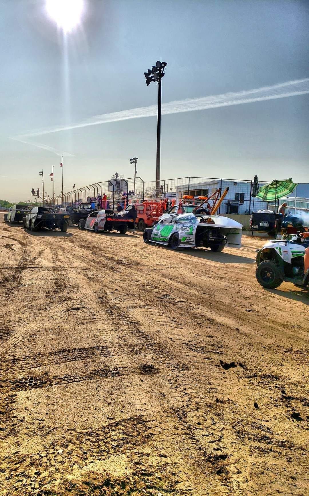 Dirt track with colorful off-road race trucks lined up at the starting area under a clear sky