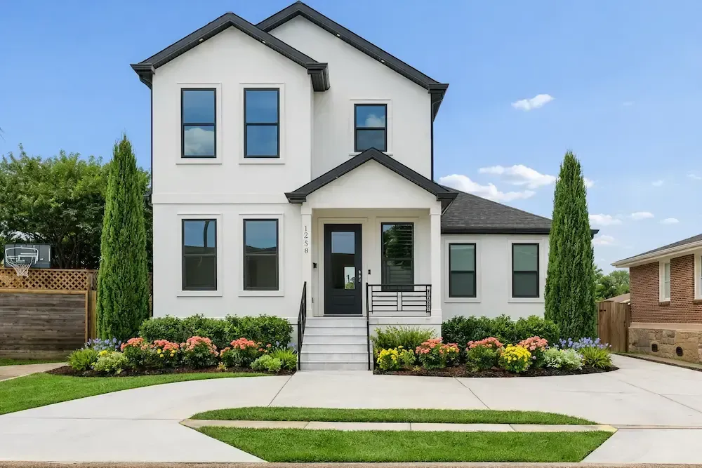 Modern two‑story white home landscaped with Taylor Junipers, Indian Hawthorne, and flowers in Lafayette, LA.