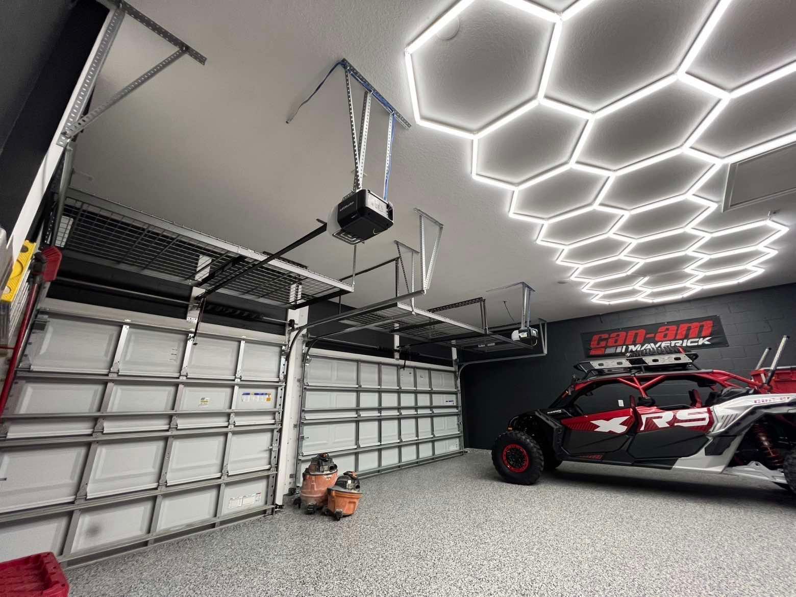 Modern garage with hexagon ceiling lights, two garage doors, and a race car parked inside.