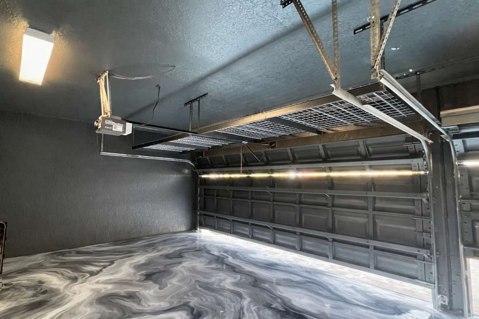 Empty modern garage interior with dark walls, gray floor, and closed black double garage door