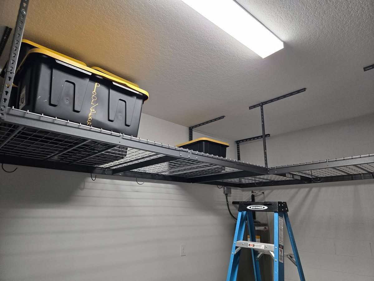 Garage ceiling storage shelves with plastic bins and a step ladder underneath