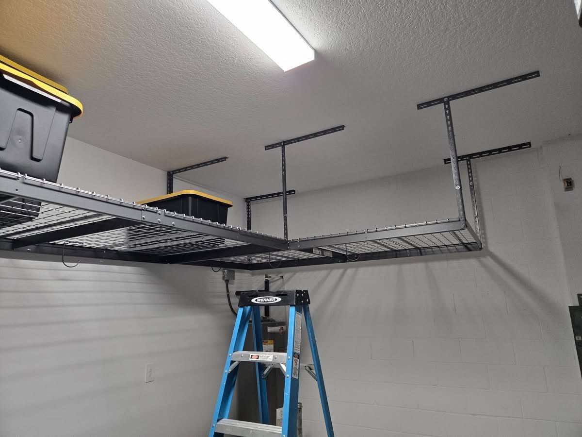 Blue ladder under black ceiling storage racks in a white garage.