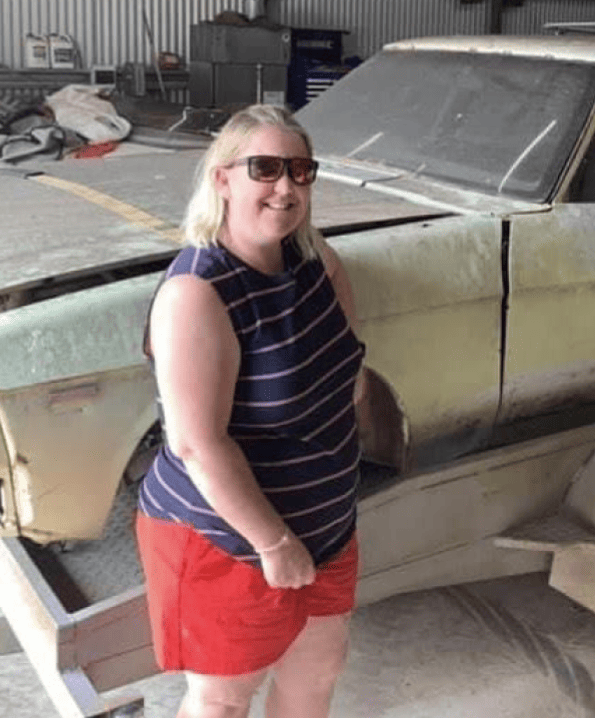 A woman wearing sunglasses is standing in front of a car