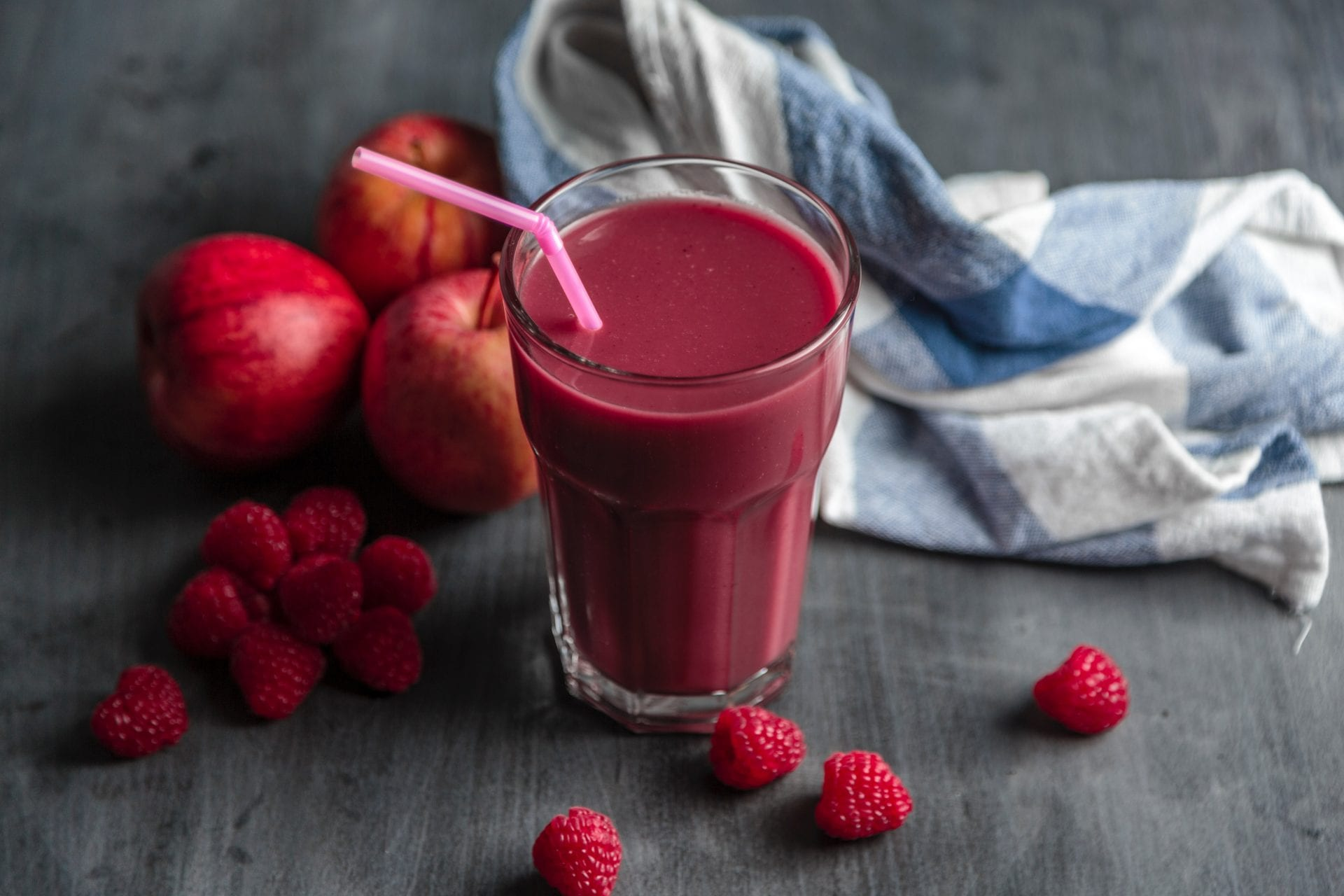 A glass of raspberry smoothie with raspberries and apples on a table.