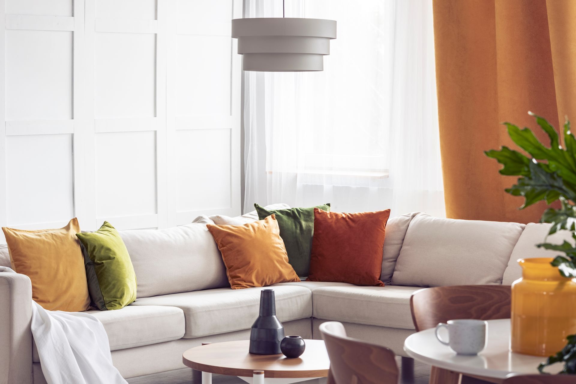 A living room with a warm color palette and layered sheer shades and drapery panels 