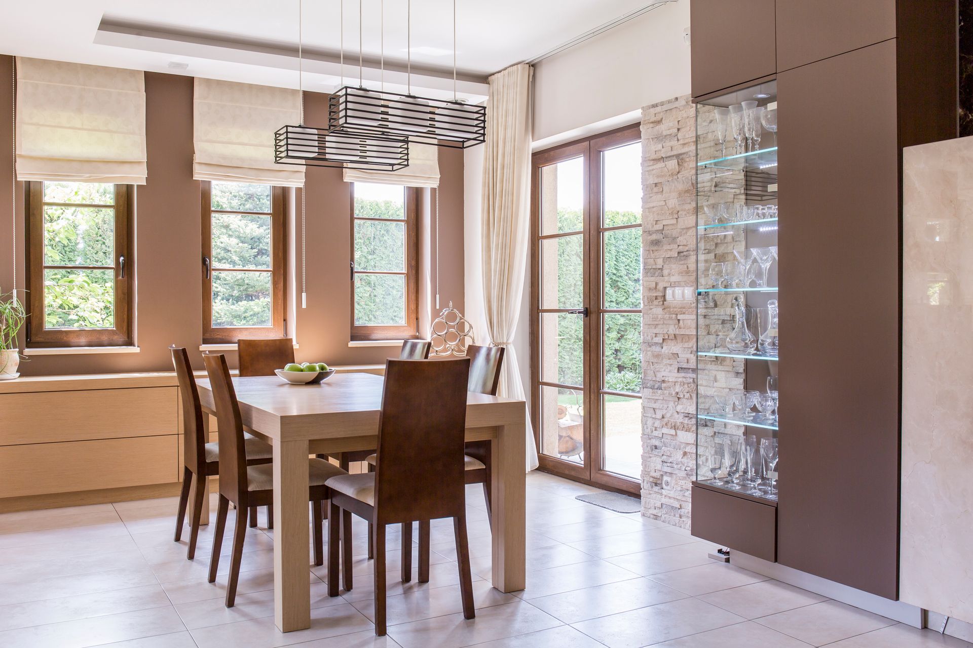 Modern, elegant dining room with custom Roman shades on windows and drapes on a door 