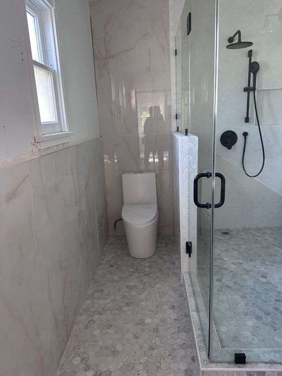 Small tiled bathroom with toilet, window, and glass shower stall.