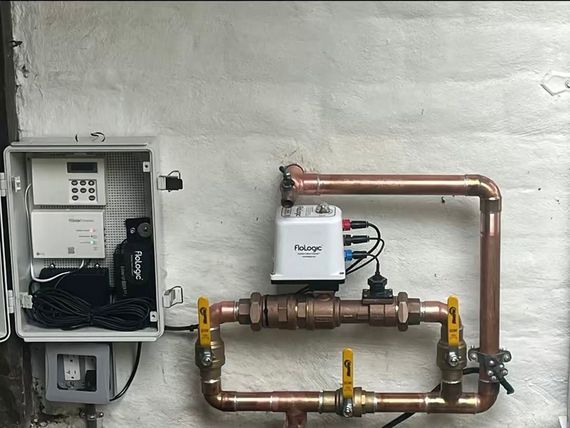 Gas meter and copper piping mounted on a white wall beside an electrical meter box.