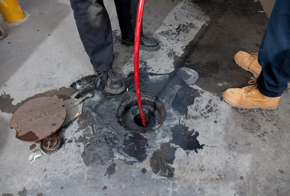 Workers using a red drain snake to clear a clogged manhole on wet pavement
