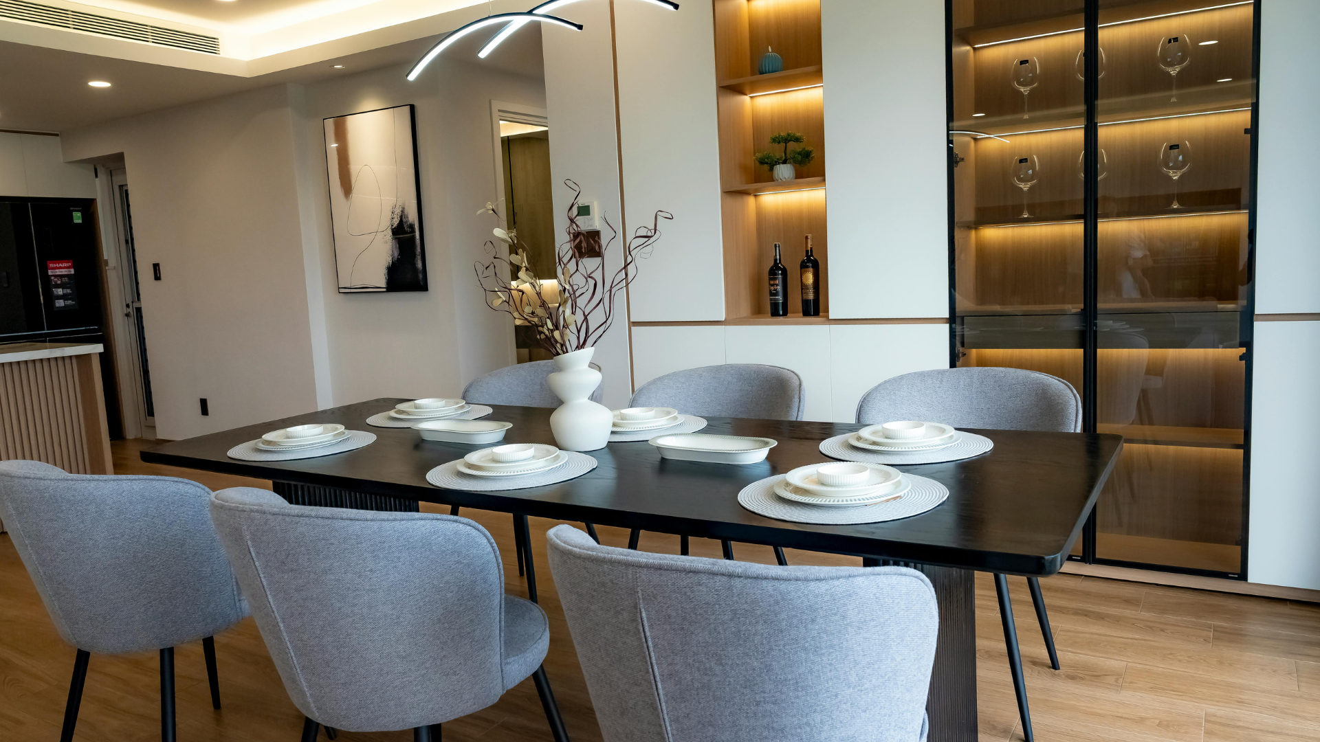 Modern dining room with a glass table, gray chairs, and built-in illuminated display shelves.