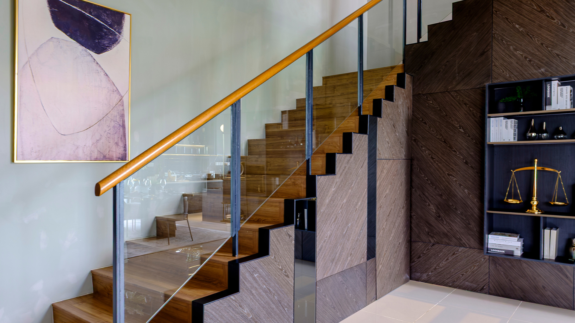 Modern staircase with glass railing, wood steps, and a wall shelf holding decor and a scale.