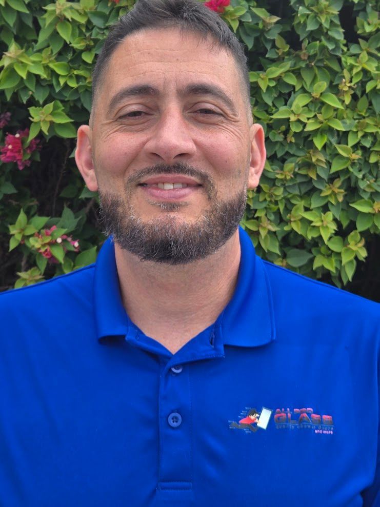 Smiling man in a blue polo shirt standing in front of green leafy foliage