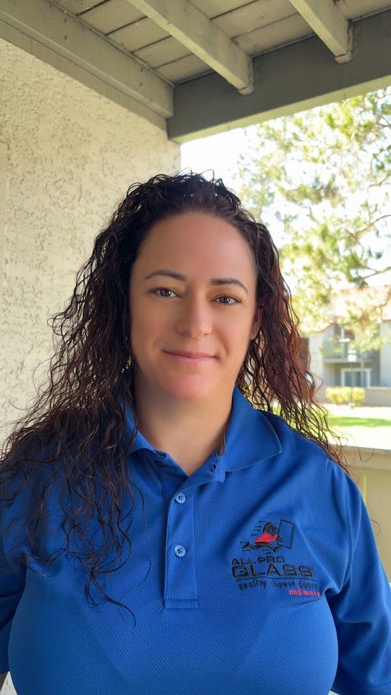 Woman in a blue polo shirt standing under a covered outdoor walkway, facing the camera and smiling.