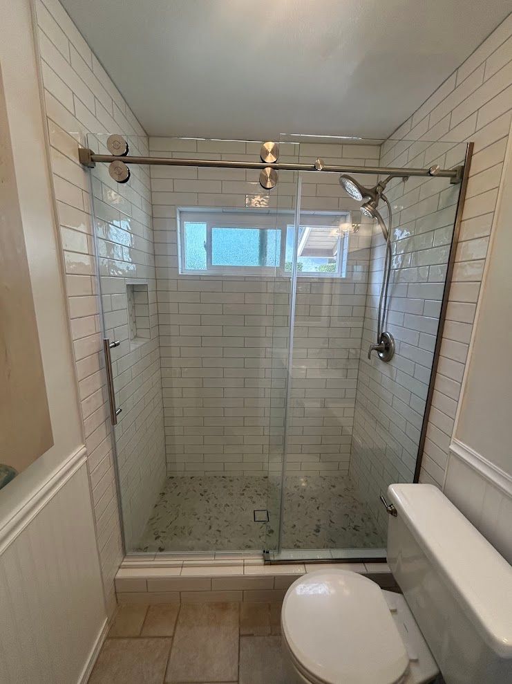 Small bathroom with a glass walk-in shower, white tile walls, and a toilet in the foreground.
