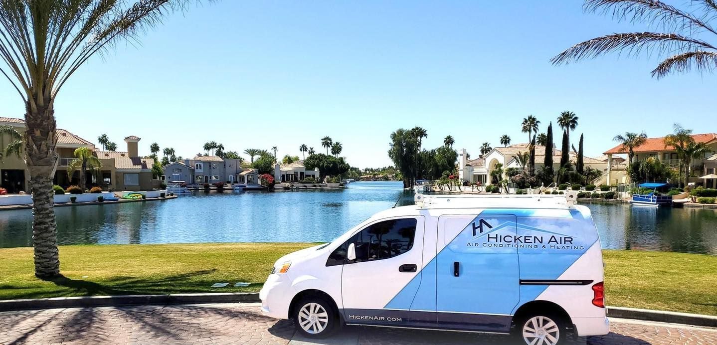 A white service van parked by a lake with houses, palm trees, and a clear blue sky.