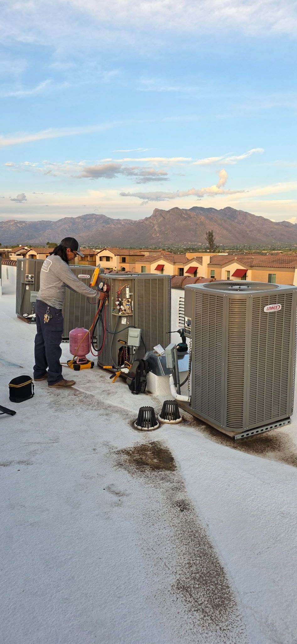 Person on a rooftop near HVAC units at sunset, with mountains and a cloudy sky in the background
