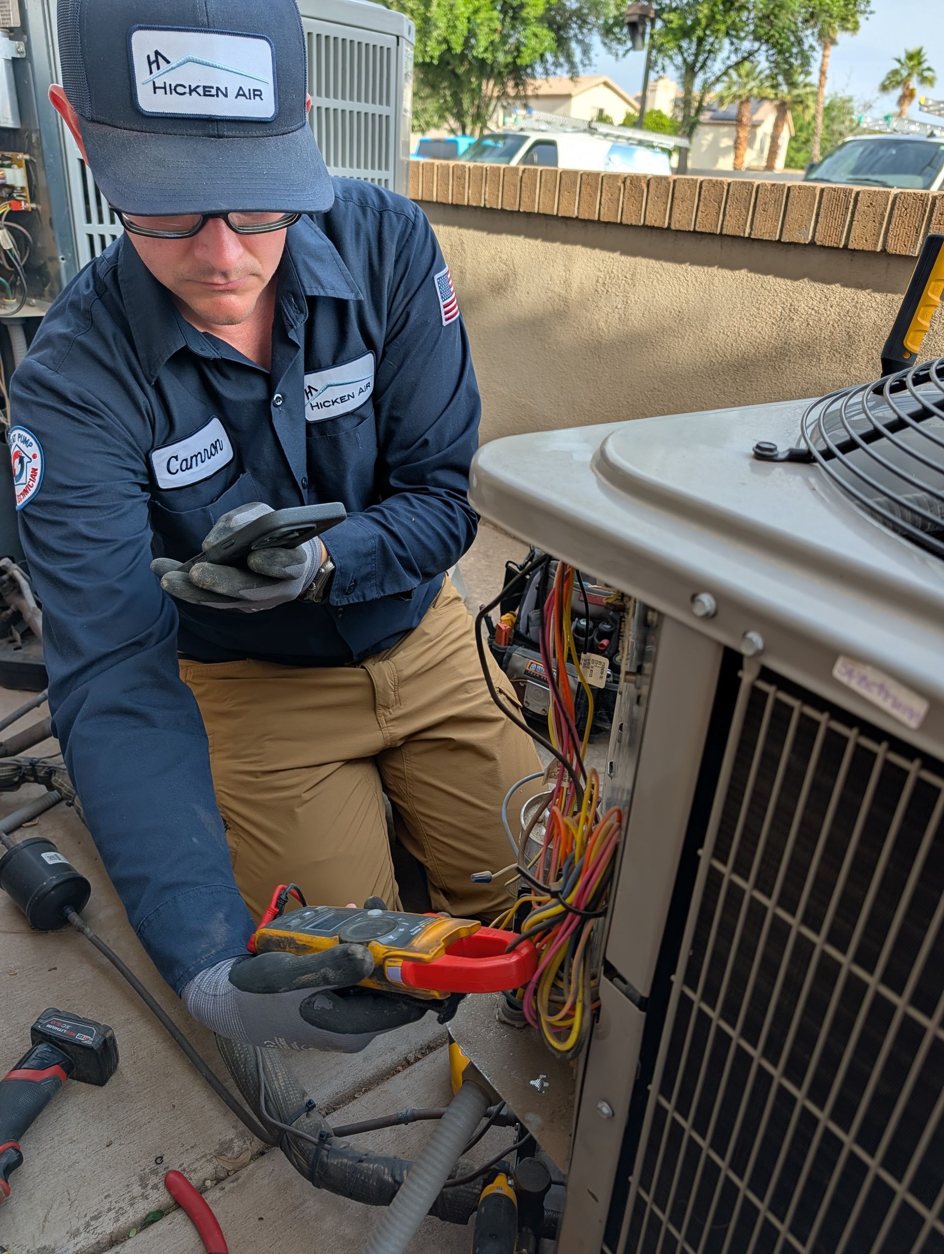 Technician inspecting wiring inside an outdoor HVAC unit, wearing a blue shirt and gloves.