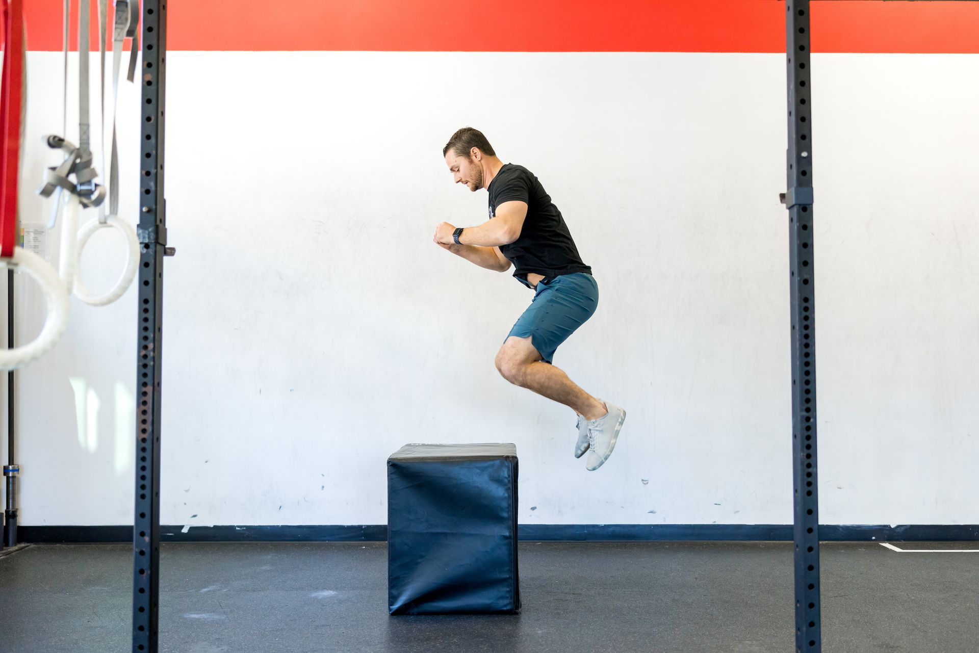 Man in gym shorts mid-jump onto black box, part of structured conditioning program at Strength Haven