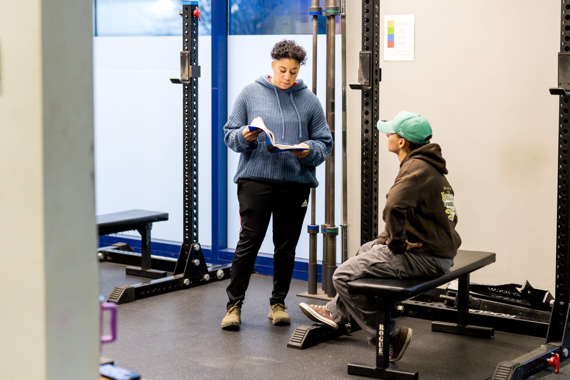 Strength Haven trainer reviews paperwork with a client seated on a weight bench during a one-on-one coaching session.
